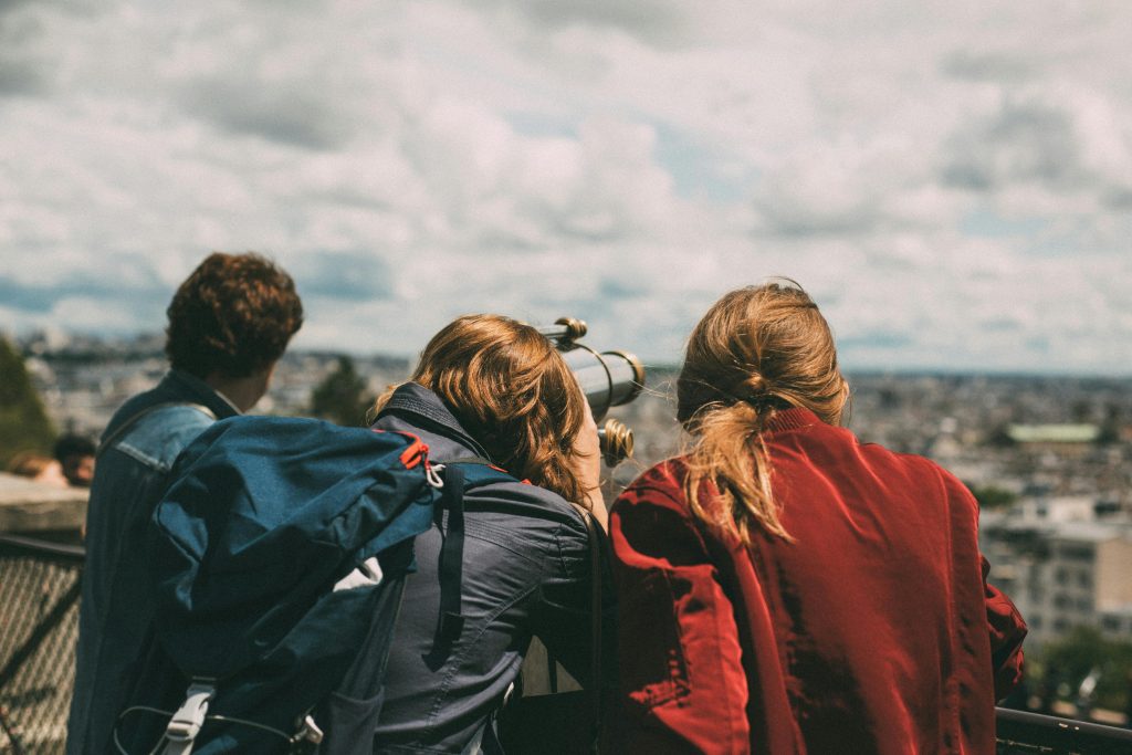 A group of young tourists exploring Paris views through a telescope during the day.